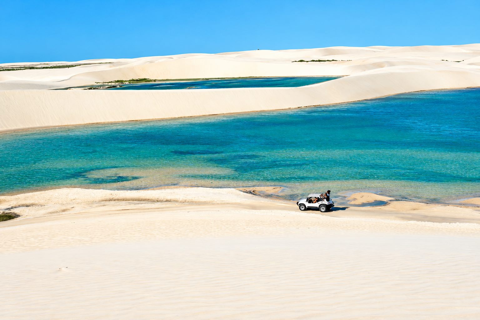 Buggy atravessando dunas brancas ao lado de uma lagoa azul